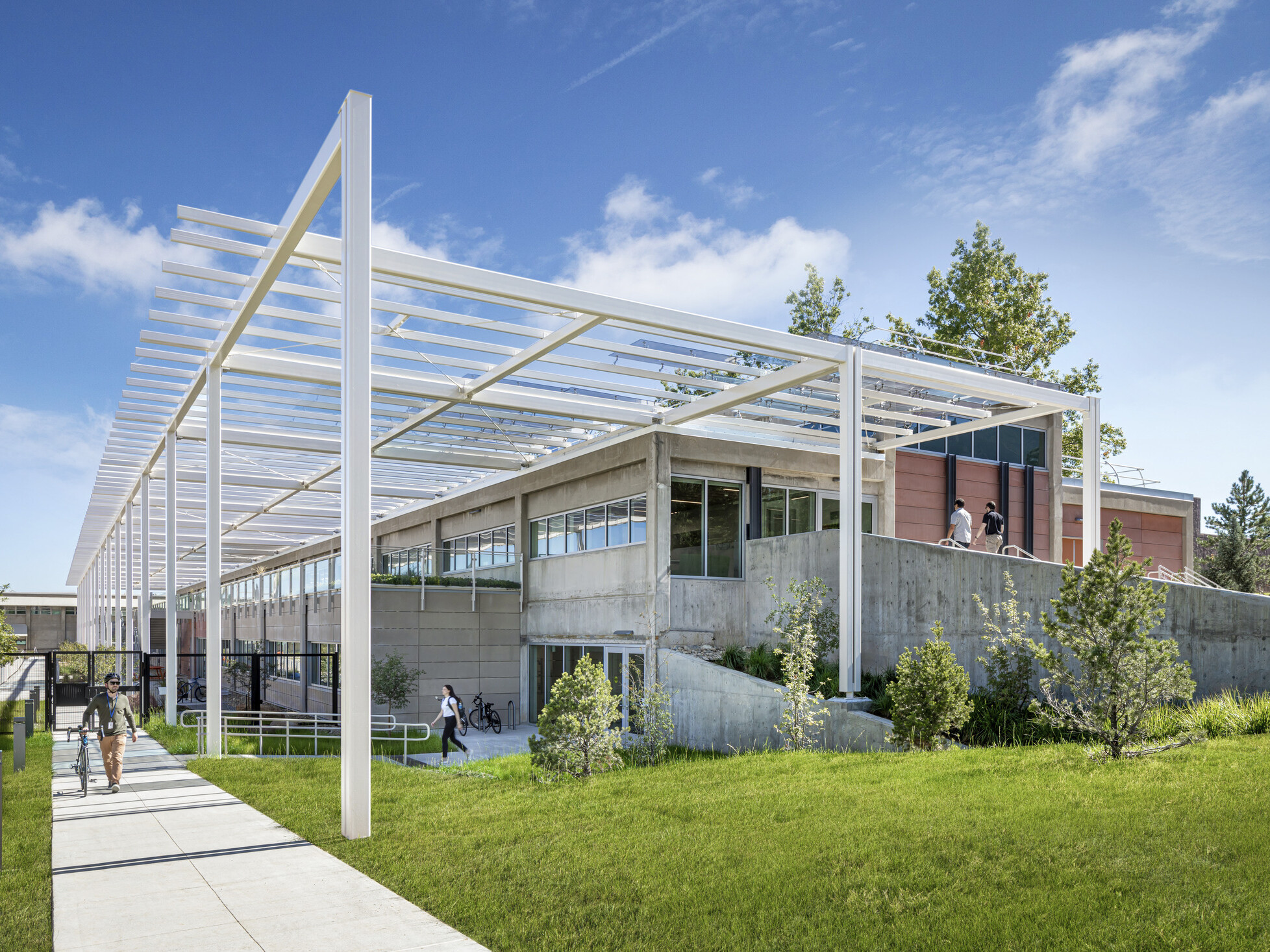 Modern multistory building built into a hill with white metal decorative columns and lush landscaping