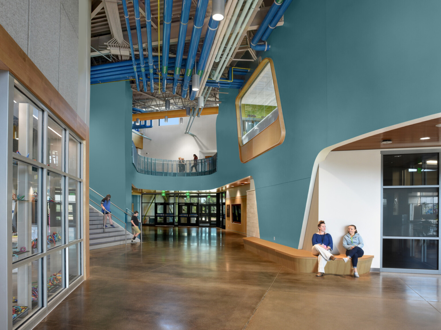 cathedral ceilings, large window that appears like a porthole to let in natural light, teal blue walls, polished concrete flooring, seating area