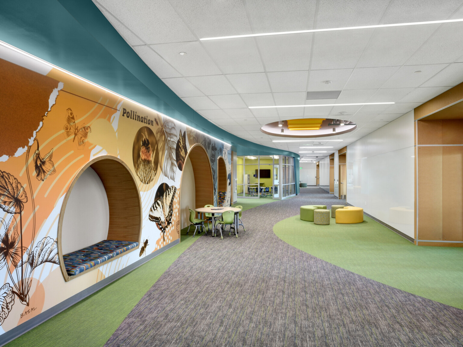 Hallway with a built-in window bench cubby, grey and green carpet appears like a road and greenbelt, lighted ceiling openings provide natural light