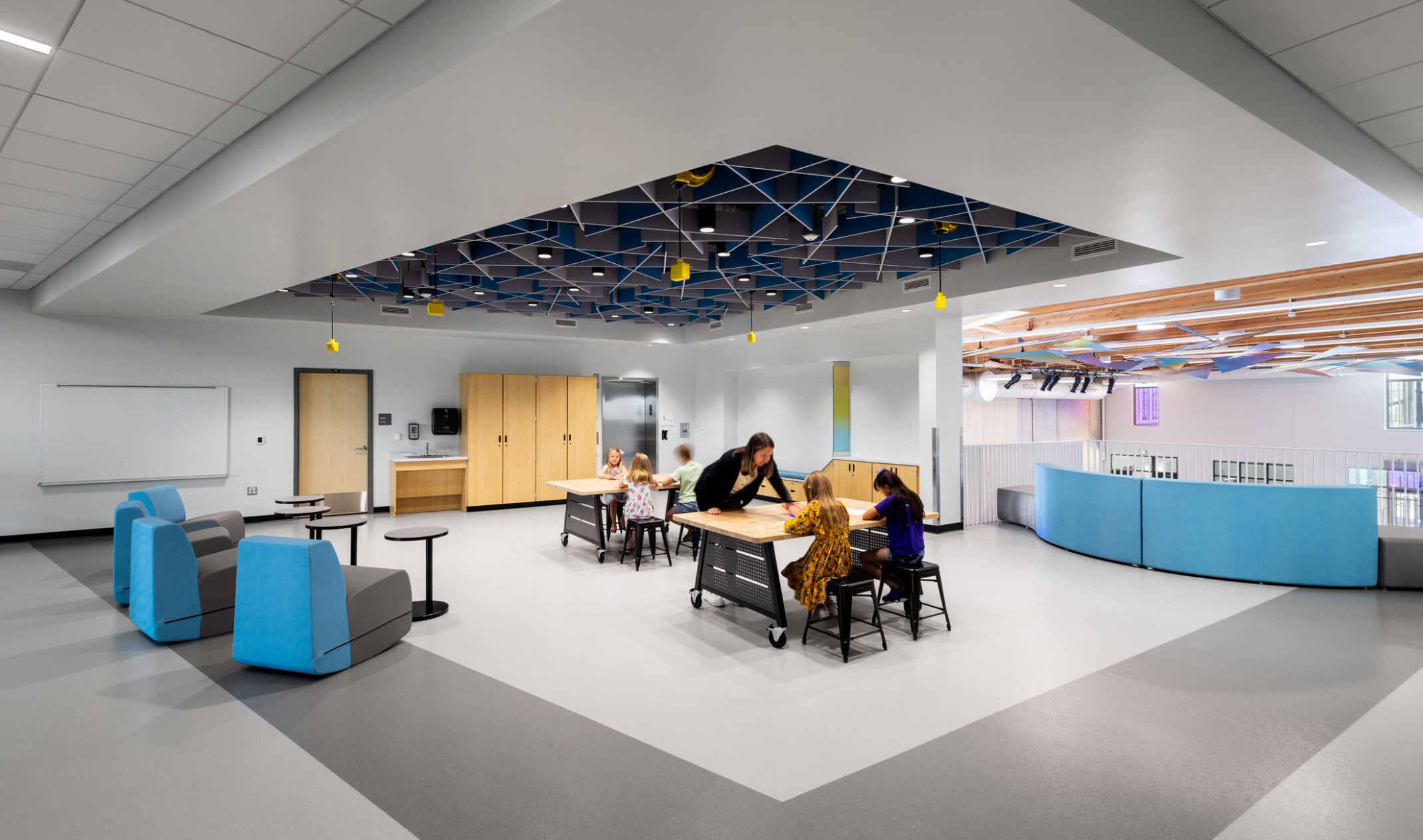Ceylon K-8 Campus open space with modular furniture and students learning at tables; teachers and students at desks; design ceiling with colorful lighting