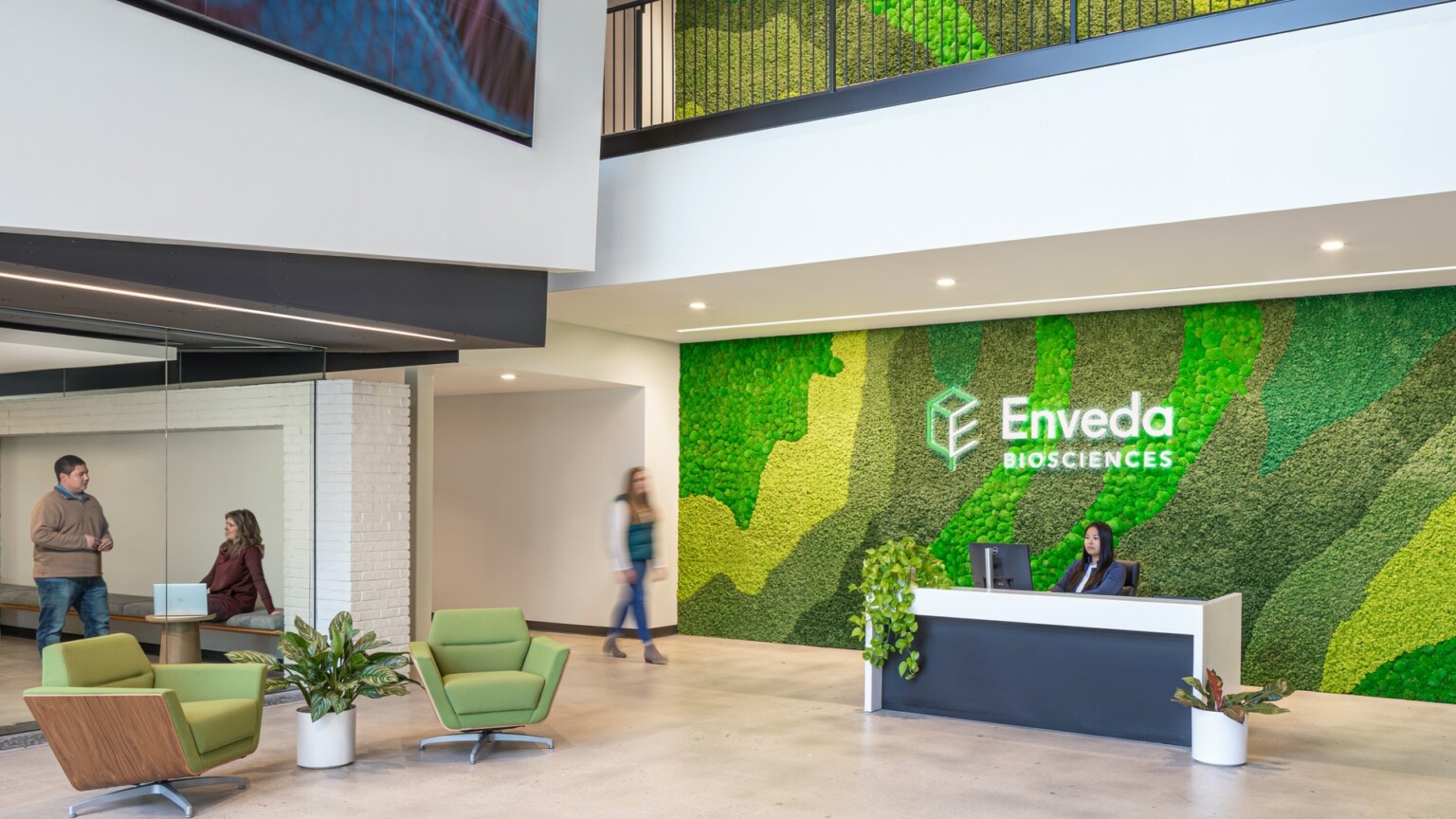 Enveda headquarters lobby; modern white sleek double height space with biophilic statement wall behind the front desk; people in the lobby, waiting area; person behind lobby desk