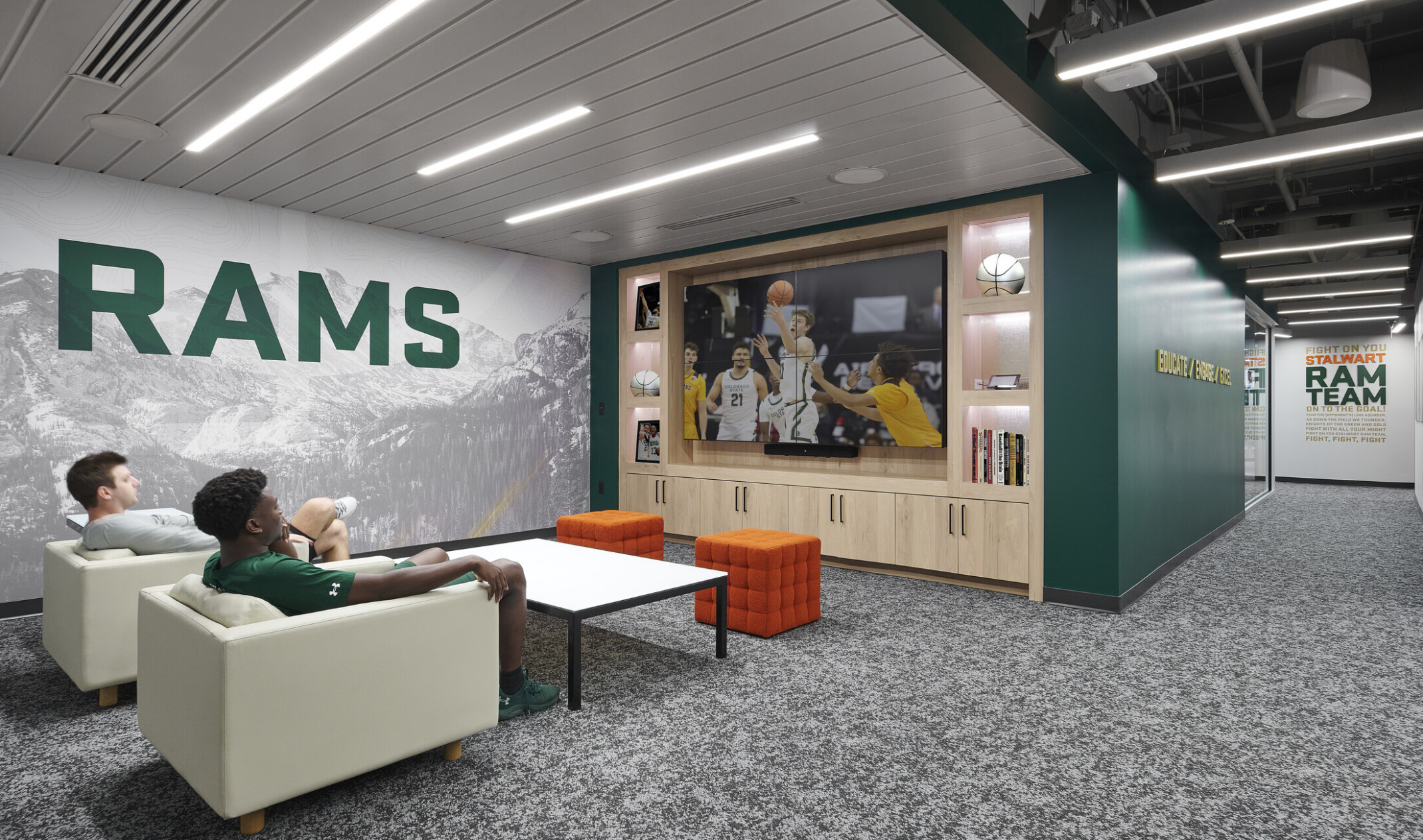 Students watching TV in a lounge area with a grey wall with the word RAMS