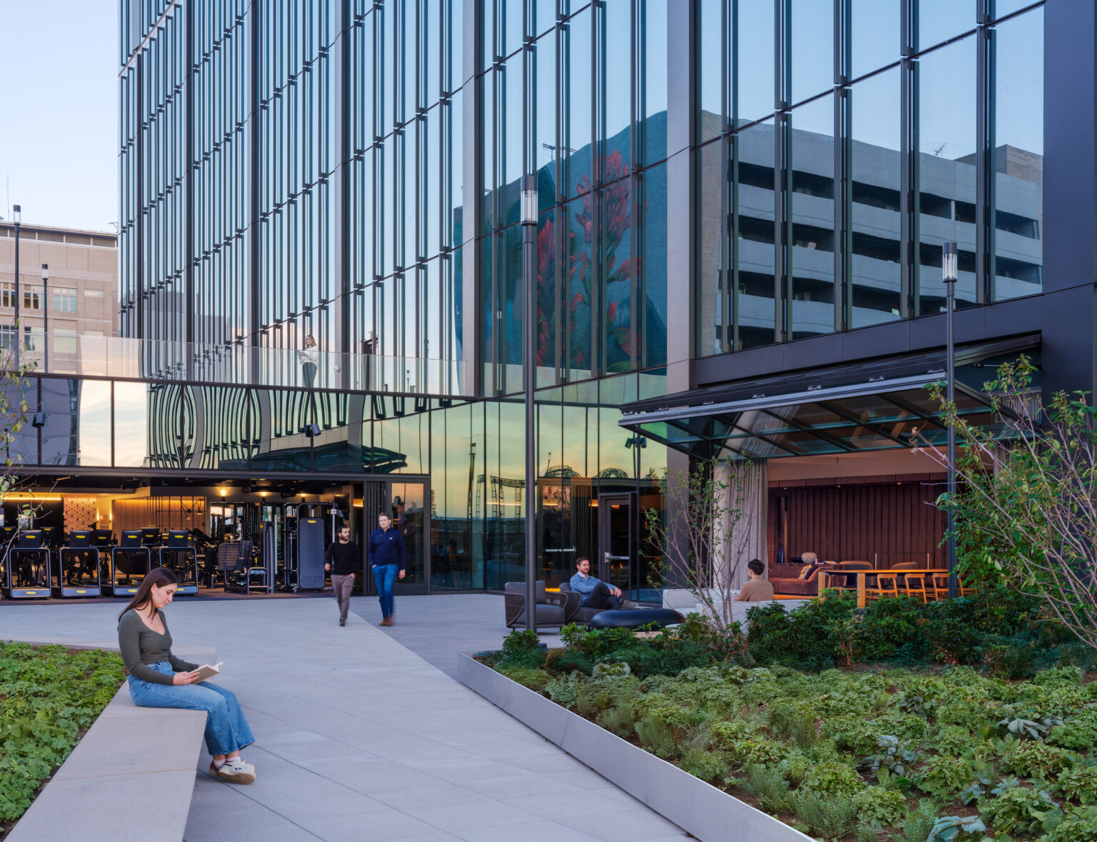 front entrance to an office building; greenery and seating as you enter into the office; woman in the front reading next to greenery