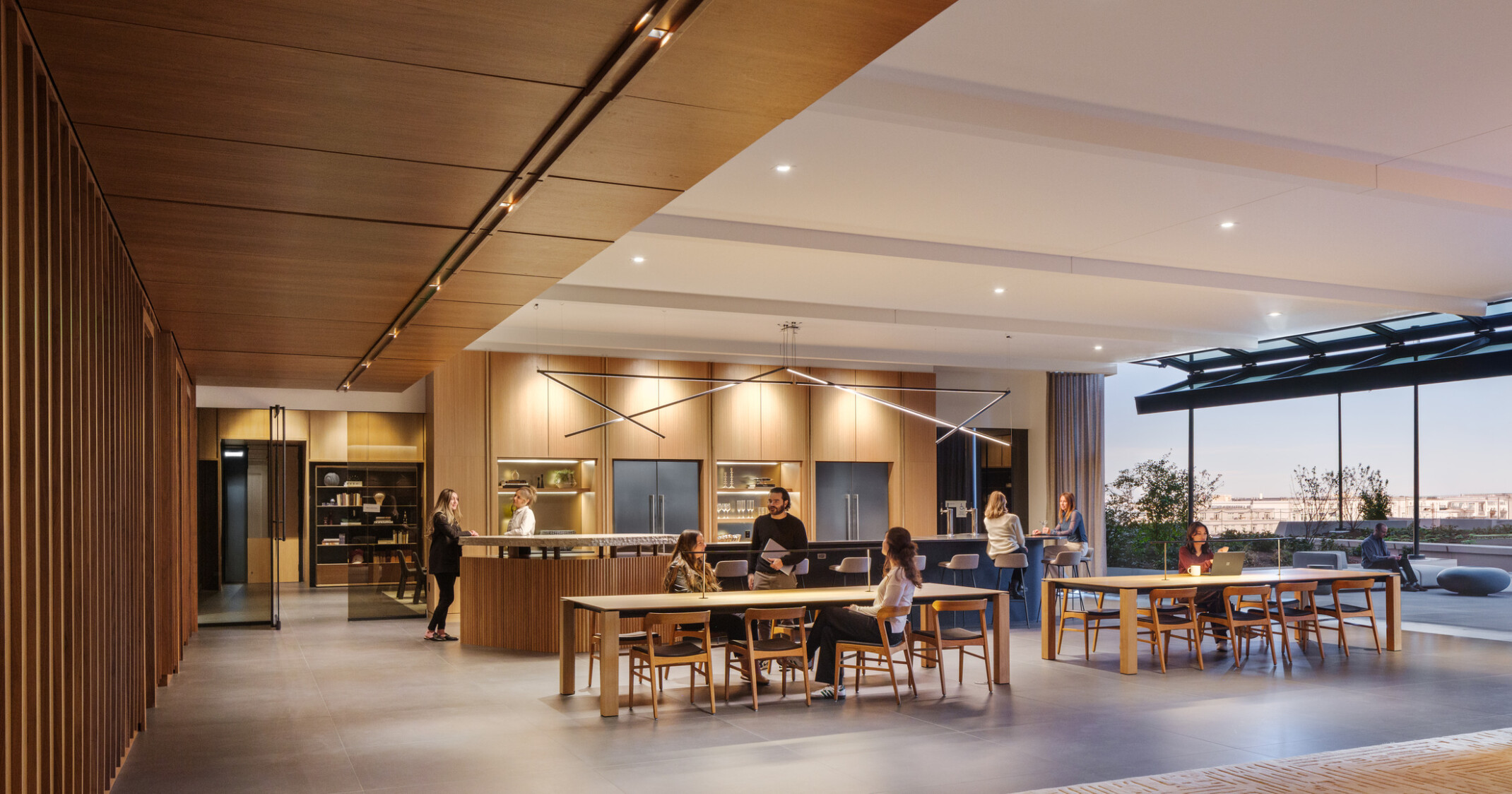 A modern office space with wooden decor, people interacting at tables, and large windows offering outdoor views.