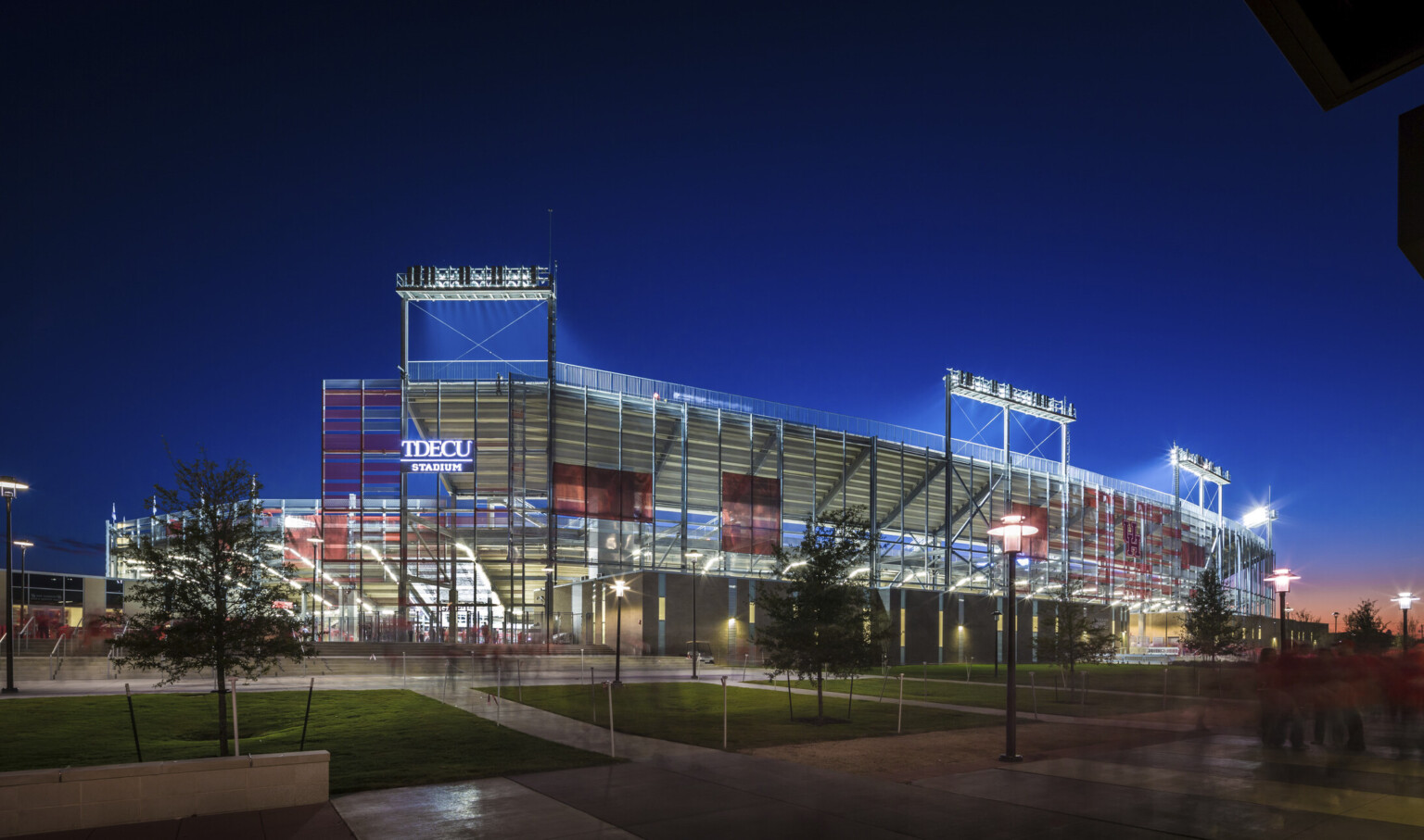 Side view of structure with TDECU Stadium sign illuminated. View through sunscreen to illuminated beams and back of bleachers
