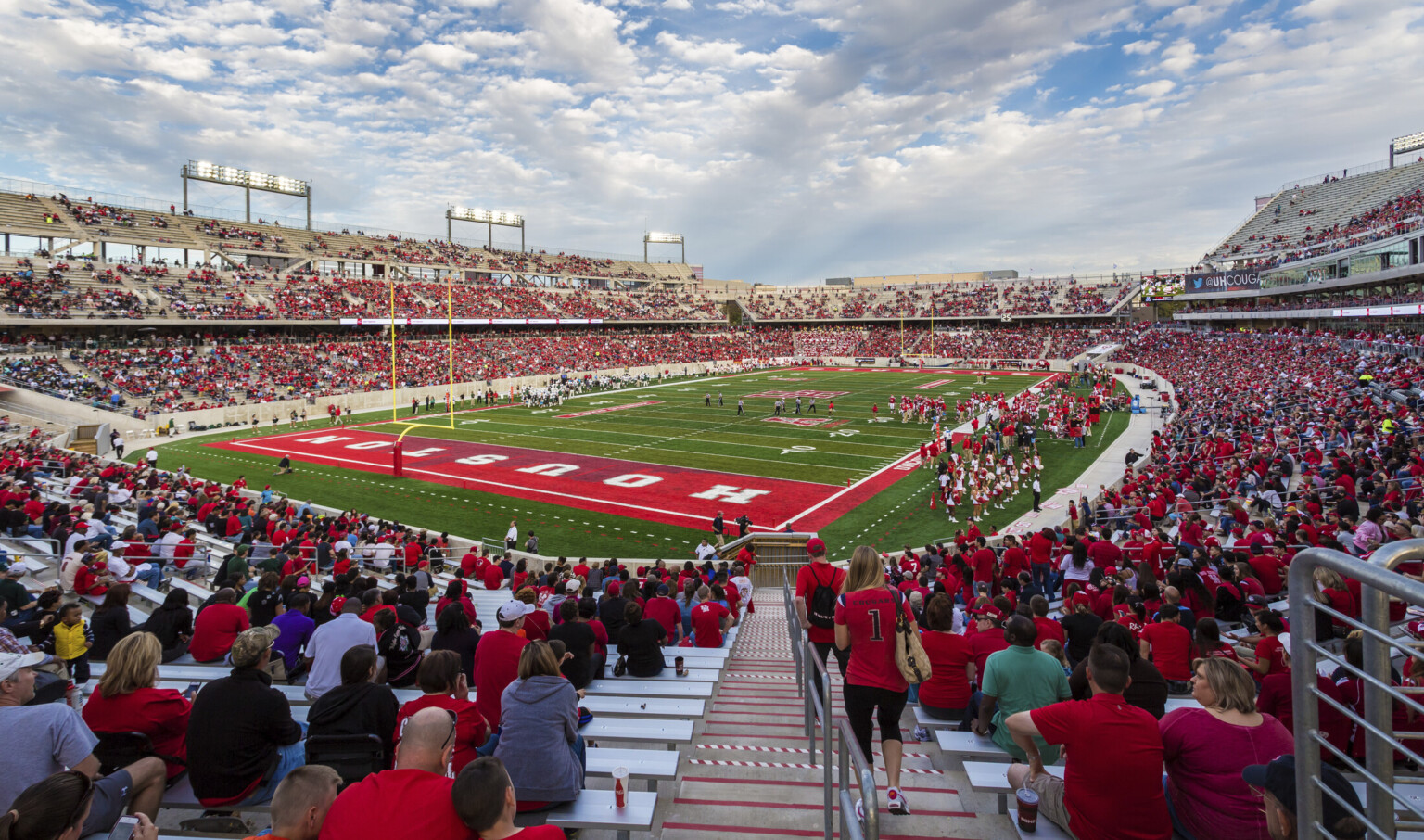 Football stadium on game day with fans in red on grey bleachers. Red end zone with Houston written in white Football stadium on game day with fans in red on grey bleachers. Red end zone with Houston written in white