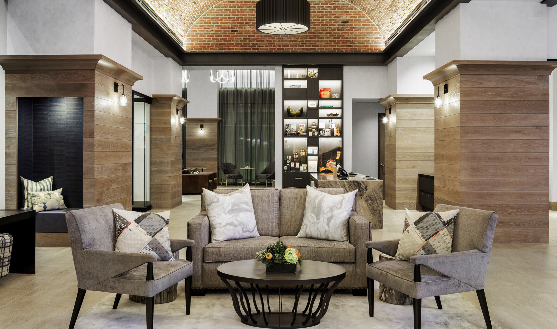 Seating area, beige couch with matching arm chairs around coffee table in white room with arching recessed brick ceiling