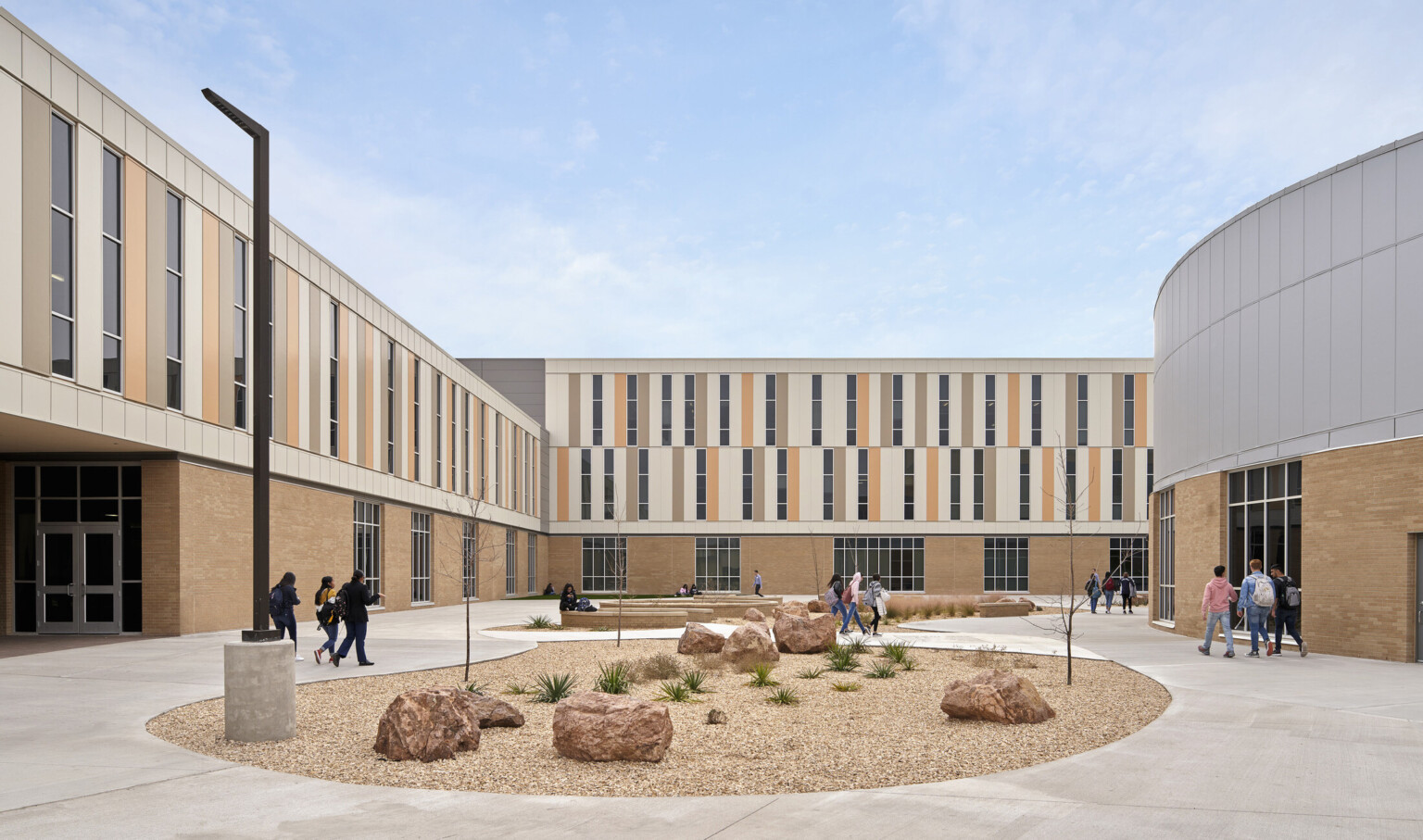 Courtyard with rock garden and organic stone benches. L shaped building at front and left, with rounded addition to the right