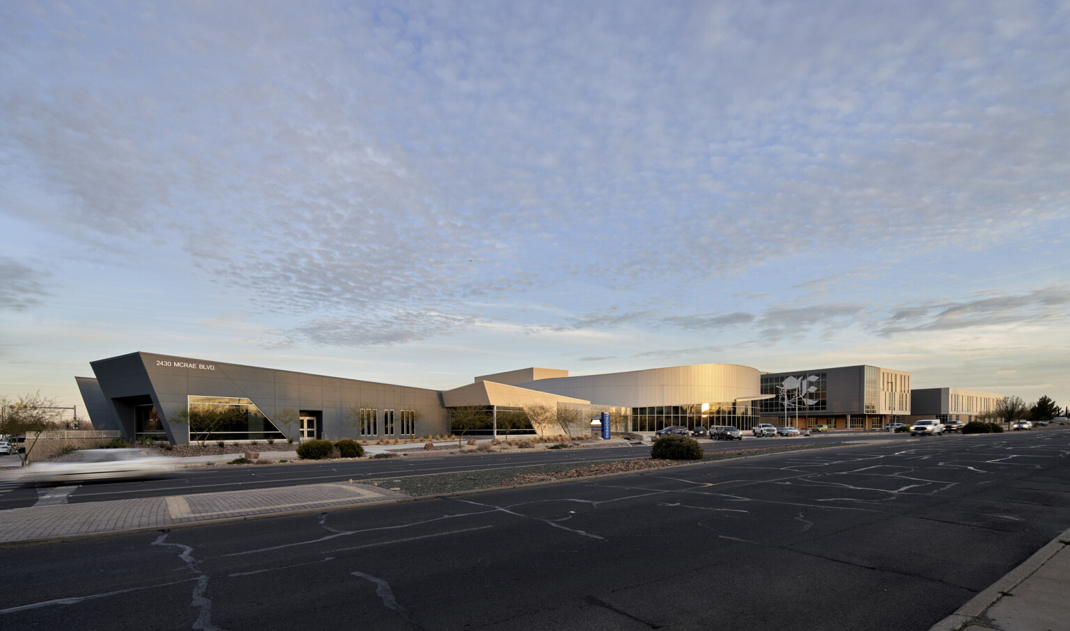 Exterior view from parking lot of angled black and white sections of building extending from rounded central structure