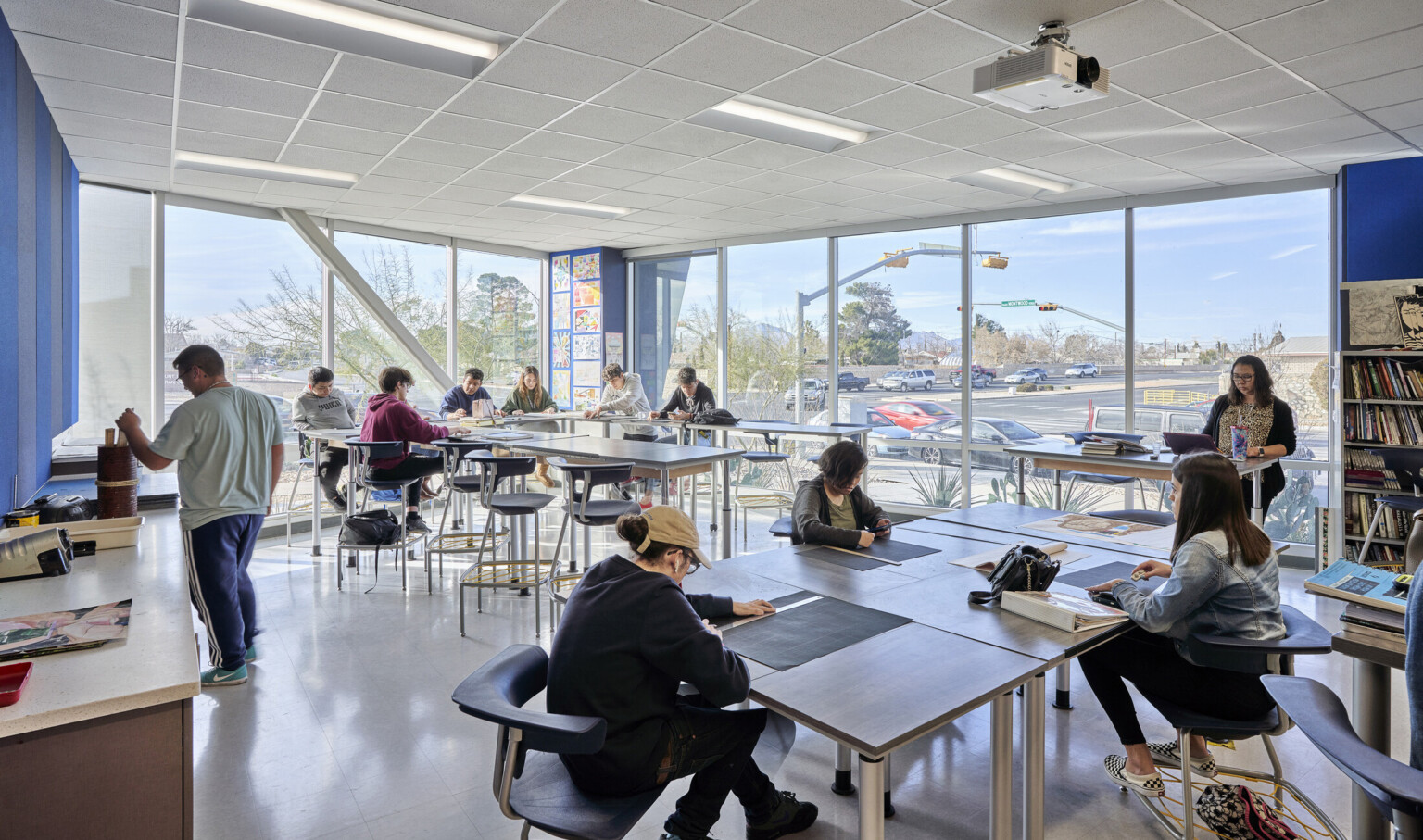 Corner art room with floor to ceiling windows looking out to street. Tables of varying heights in a room with blue walls