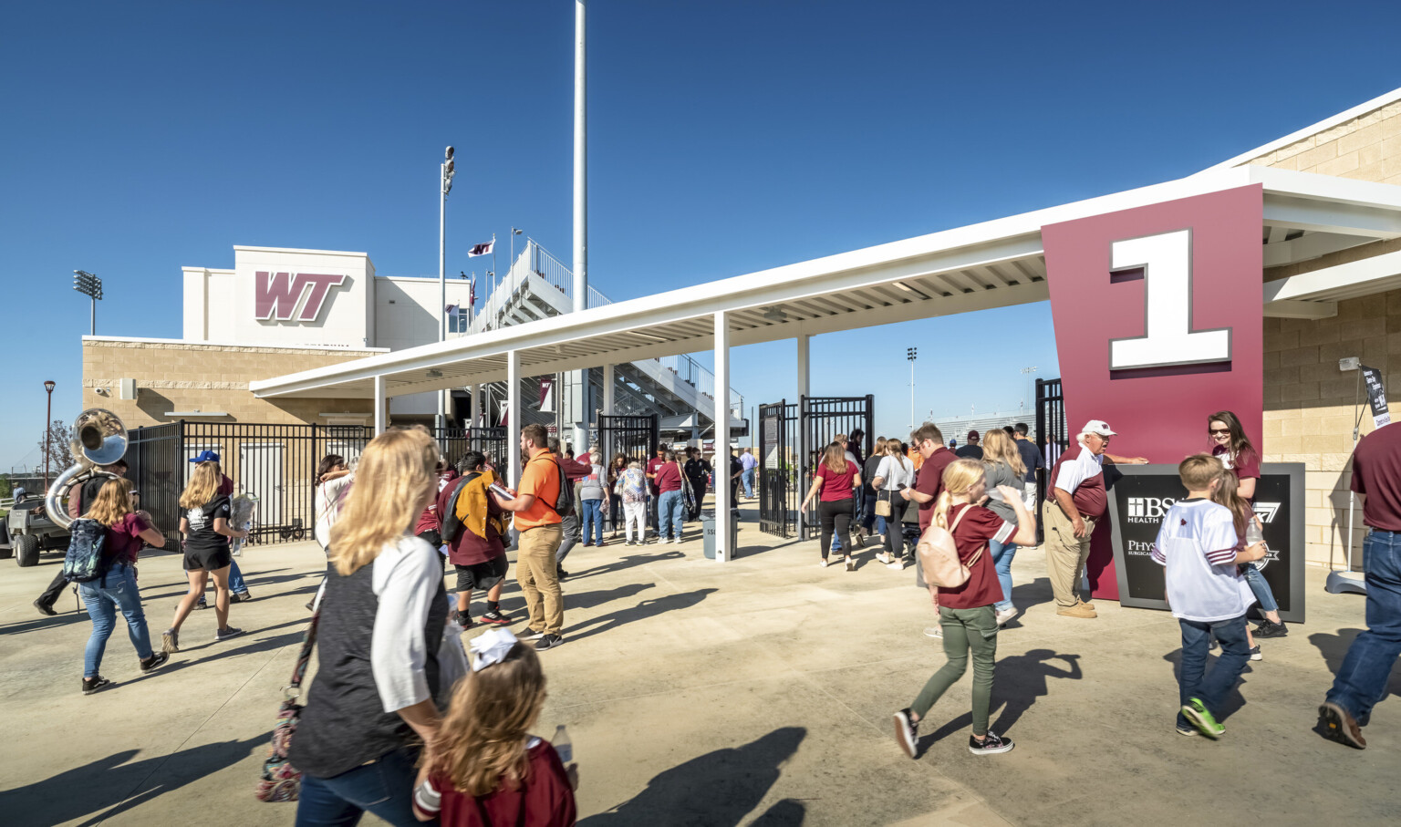 Gated entrance to stadium labeled 1 in white font on red angled panel to right. Canopy over entry connecting to building
