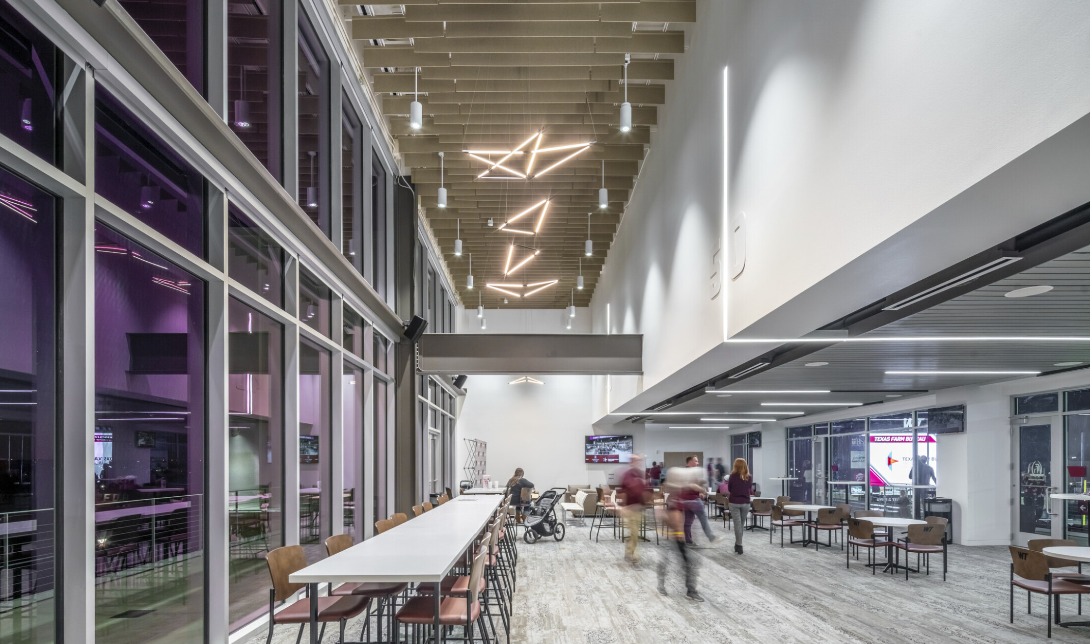 Double height hallway with wood slat ceiling and sculpture light fixtures. Purple translucent windows to left, seating areas