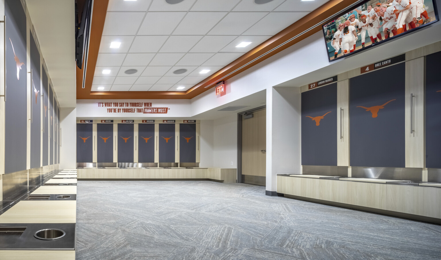 Locker room with orange logo on recessed grey lockers. White room with recessed ceiling framed by orange border