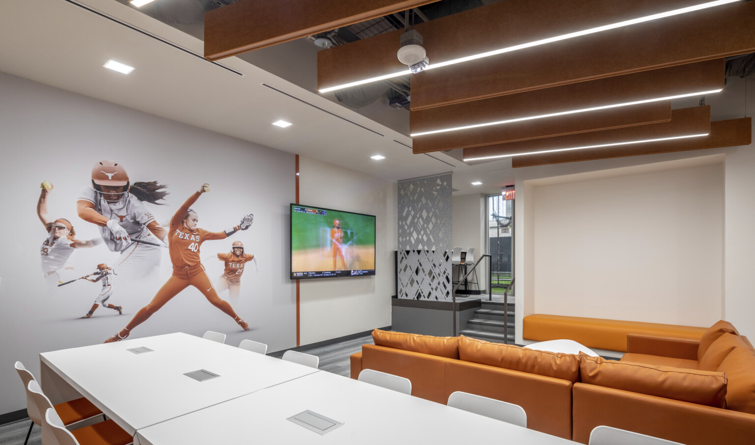 University of Texas Softball Development Facility interior. Softball mural on wall next to screen in front of orange couch