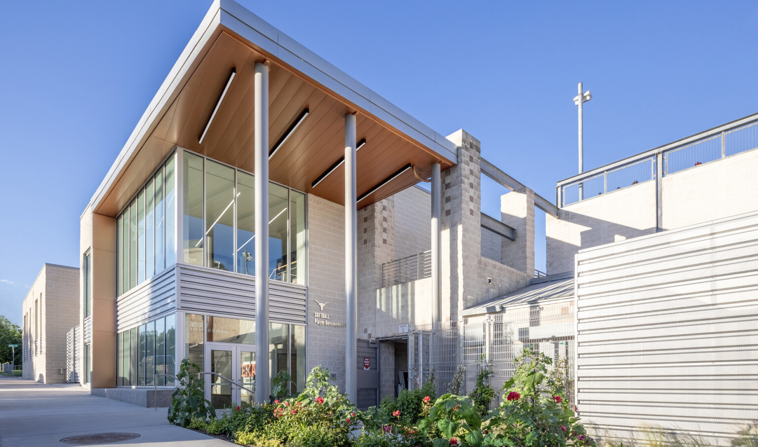 Corner view of white panel building with glass front and partial side. Wood base on canopy wrapped facade with white columns