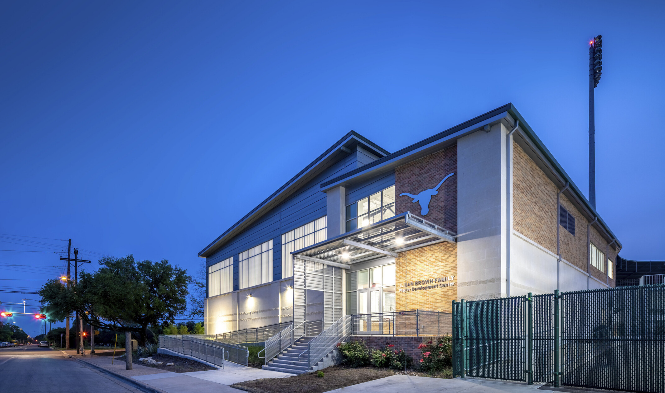 Corner view of brick building with white wrap facade. Connected white panel building with angled roof, left. Sheltered entry