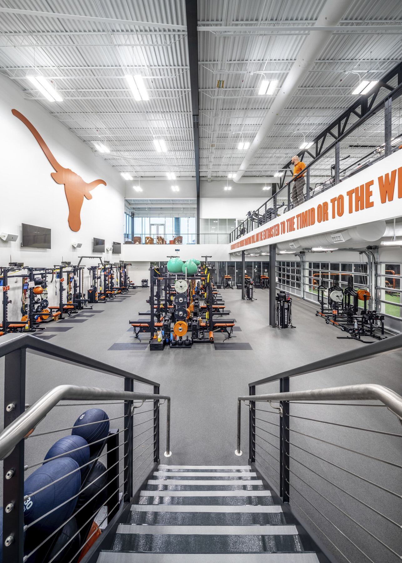 Looking down center row of equipment in double height white room. Screens and orange longhorn mascot logo on left wall