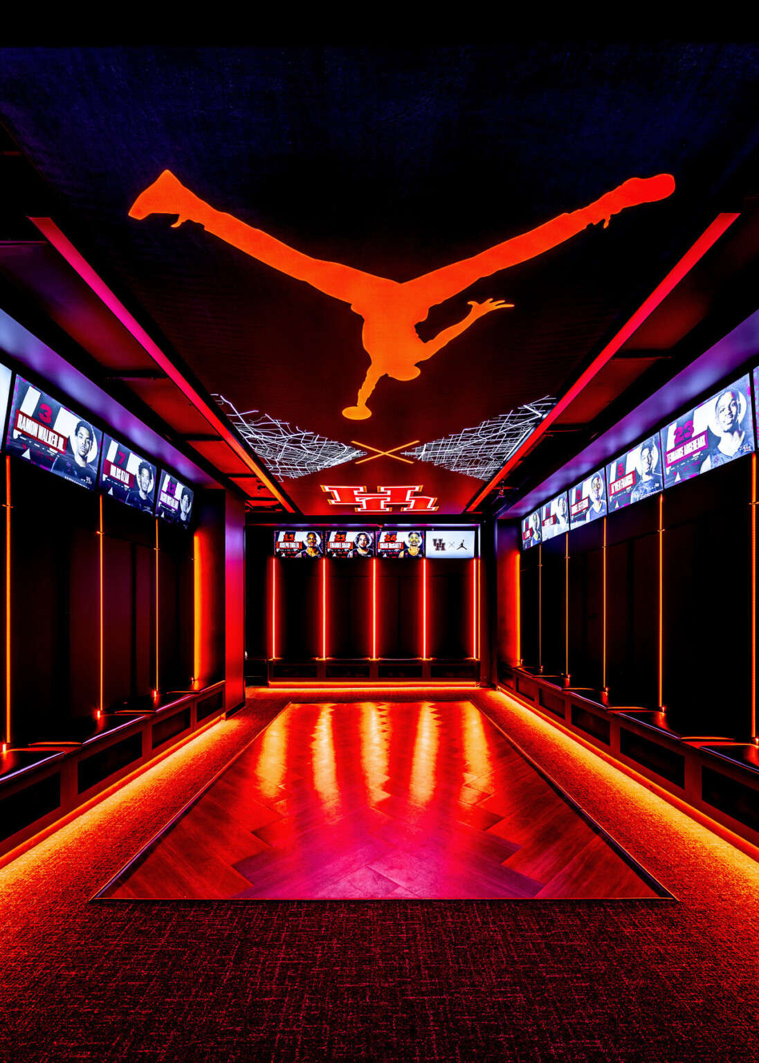 Basketball locker room with red lighting along the ceiling and floors with a red Jumpman on the ceiling. Digital screens with players photo and name above the lockers
