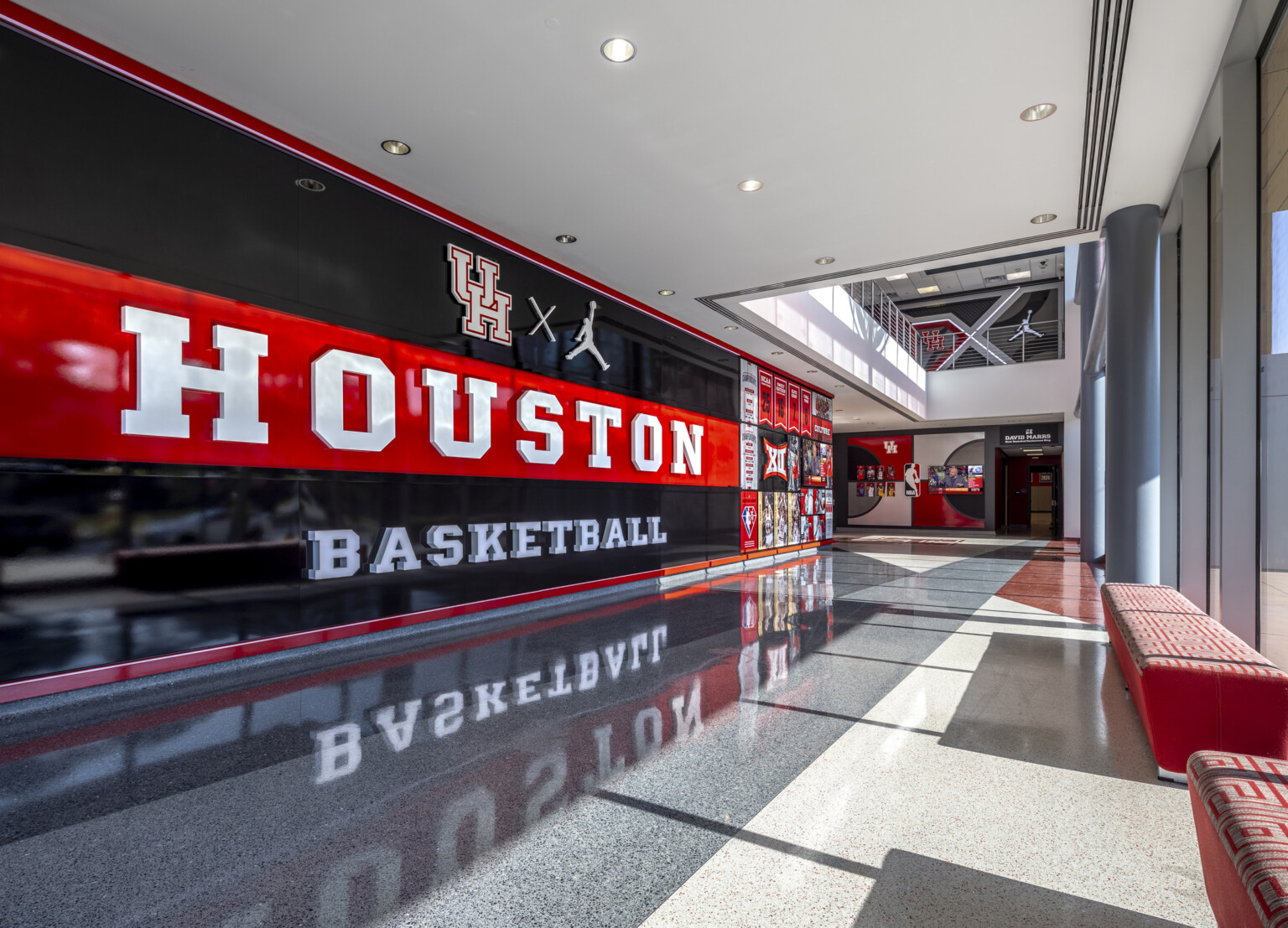 Spacious hallway with a "HOUSTON BASKETBALL" mural, reflective floors, and large floor to ceiling windows