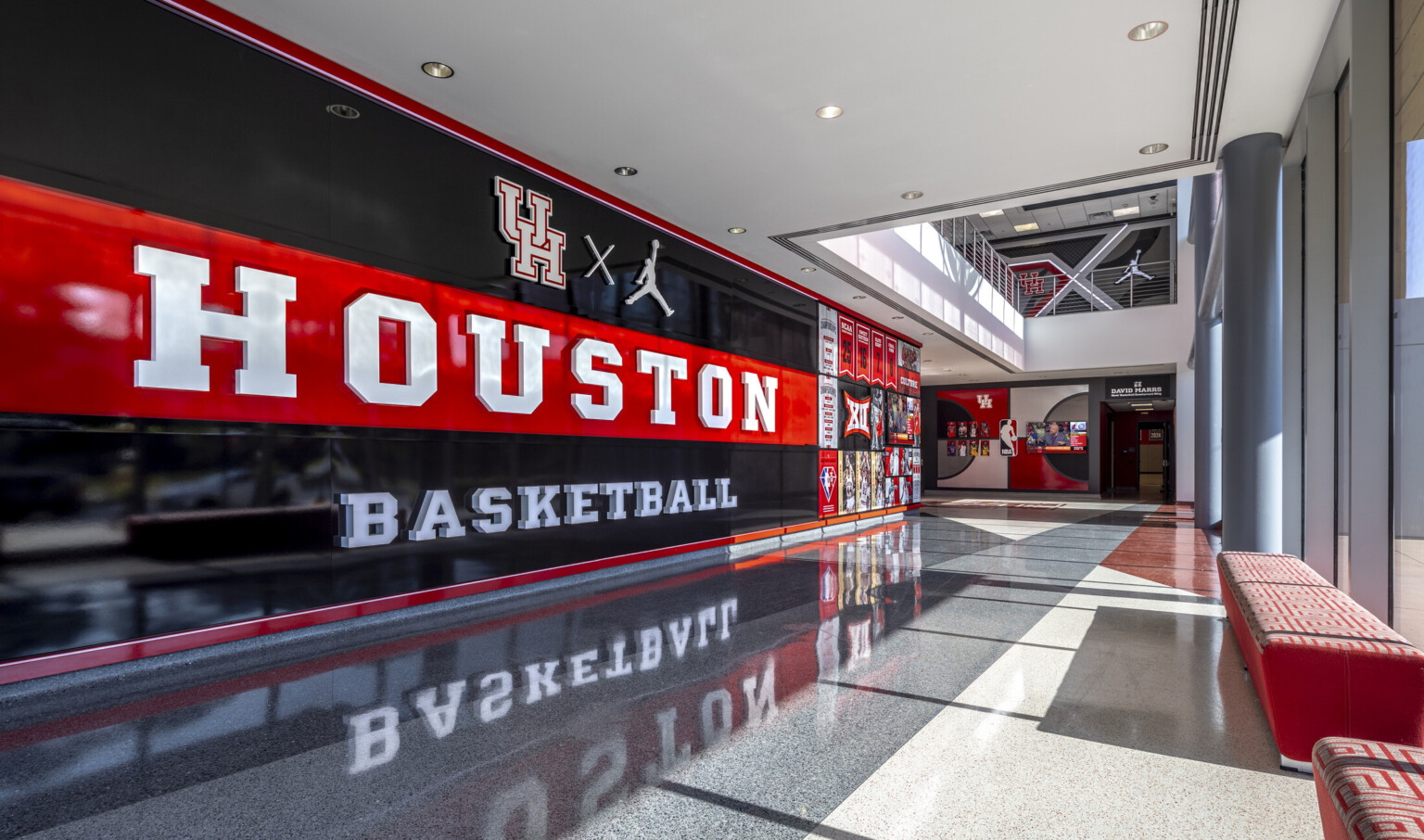 Spacious hallway with a "HOUSTON BASKETBALL" mural, reflective floors, and large floor to ceiling windows