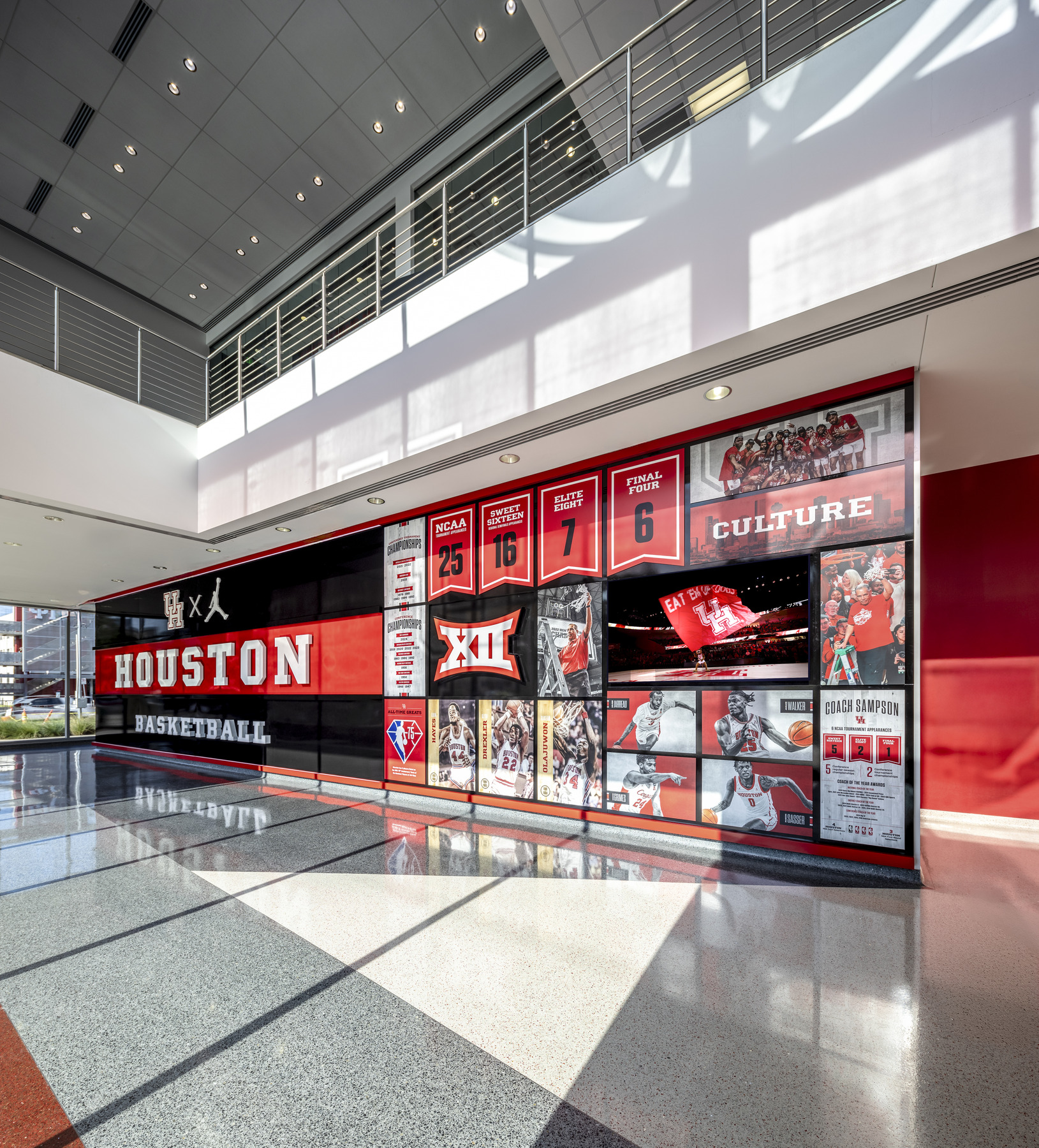 interior of a sports facility; Large black and red "HOUSTON" wall with sports collage of athletes. coaches, awards. stats