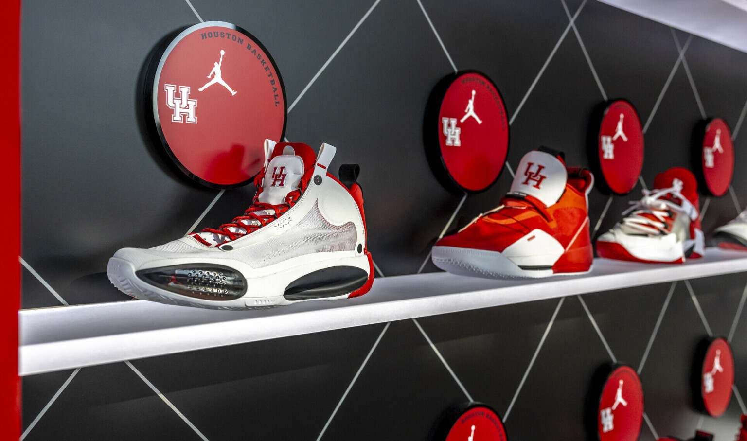 Display of athletic shoes on shelves with round red plaques featuring "UH" and the Jordan logo