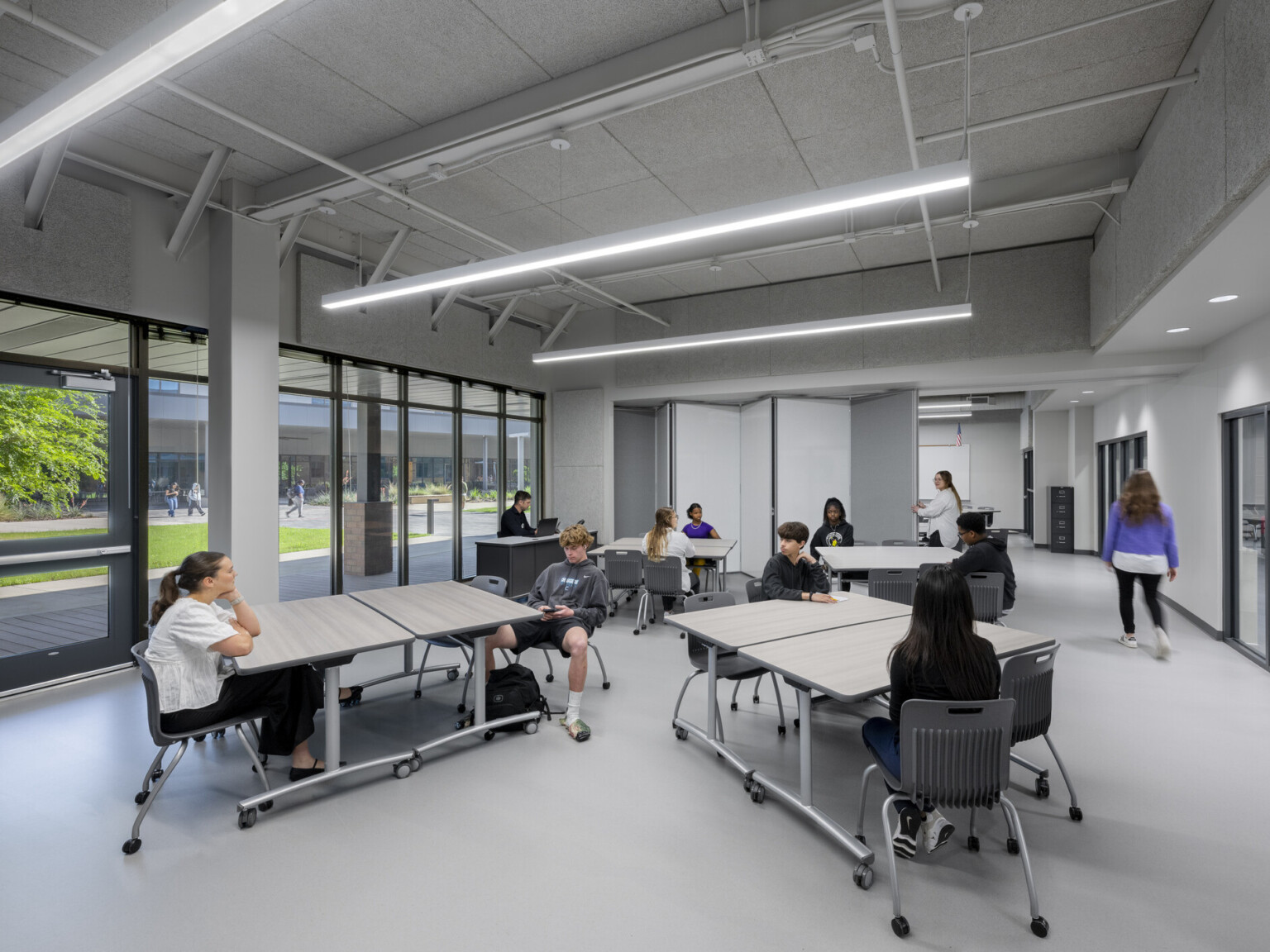 Classroom filled with grey tables and black chairs. Large windows overlooking the outdoors on the left side Classroom filled with grey tables and black chairs. Large windows overlooking the outdoors on the left side