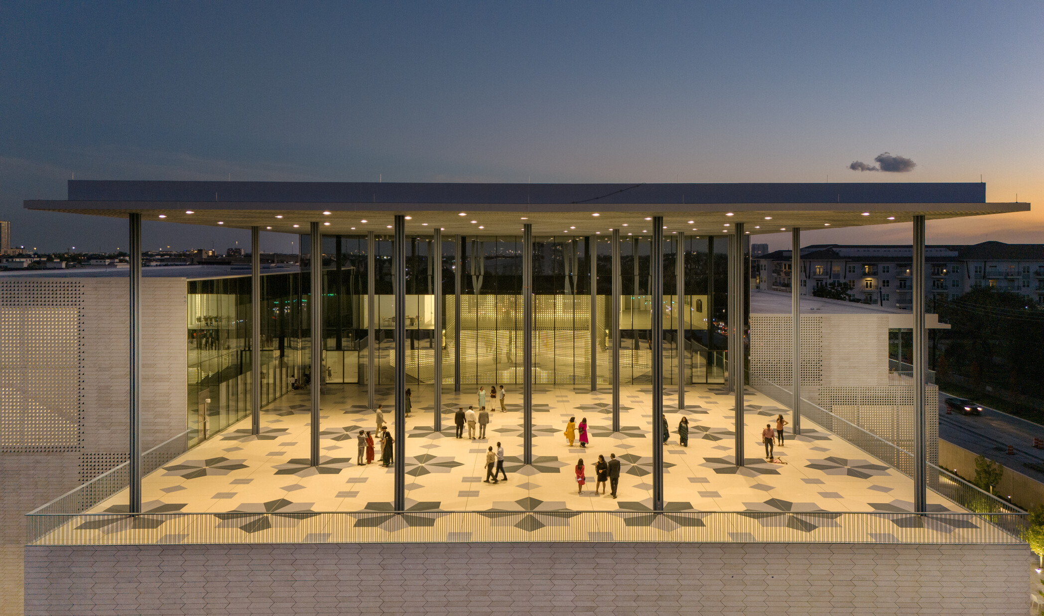 A modern building at sunset with a large, covered veranda supported by columns. Geometric patterns adorn tile floors.