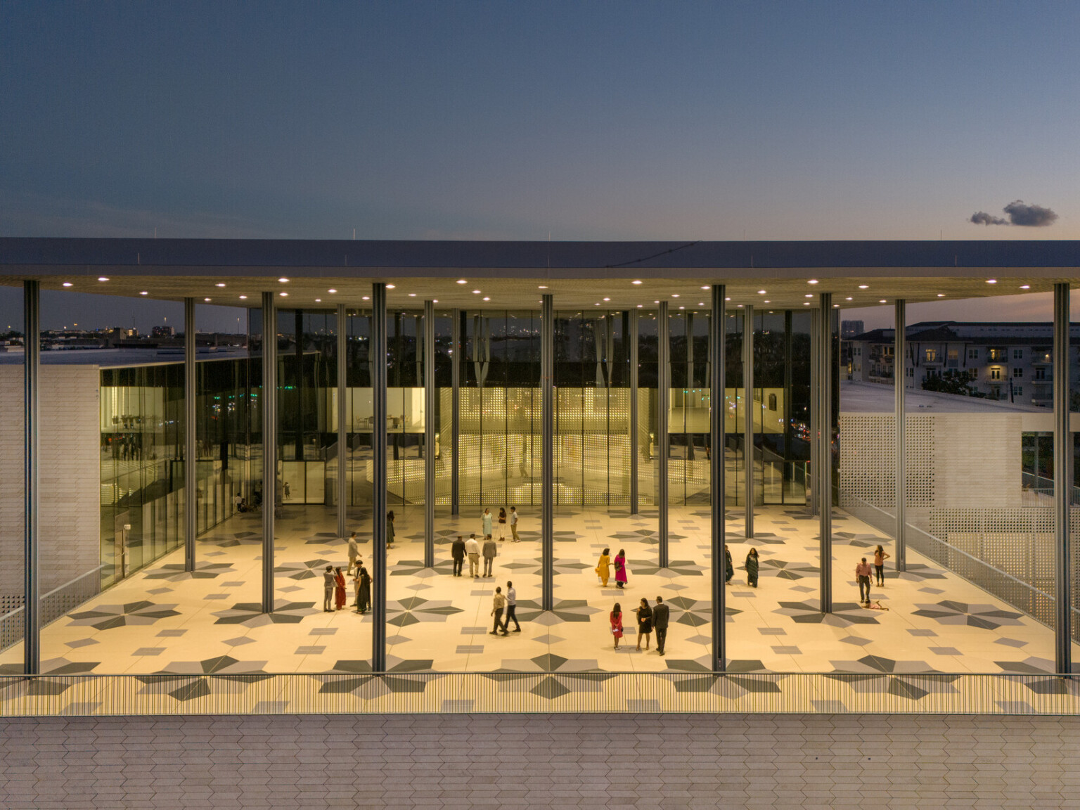 A modern building at sunset with a large, covered veranda supported by columns. Geometric patterns adorn tile floors.