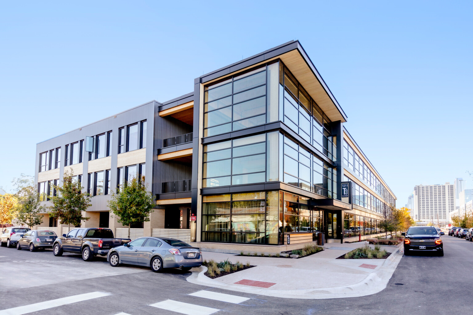 Corner view of building with black exposed steel at front, white ribbed panel, back, exposed mass timber and large windows, greenery