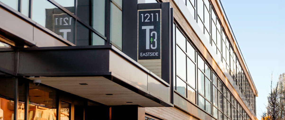 Side view of building with black exposed steel, exposed mass timber and large windows with a T3 sign