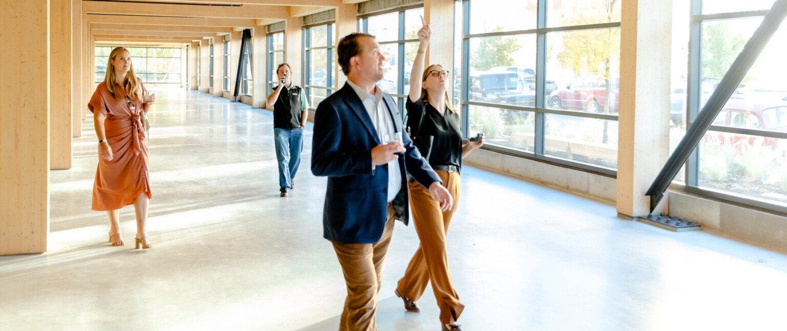 Multiple business people walking through a hallway with windows on the right side