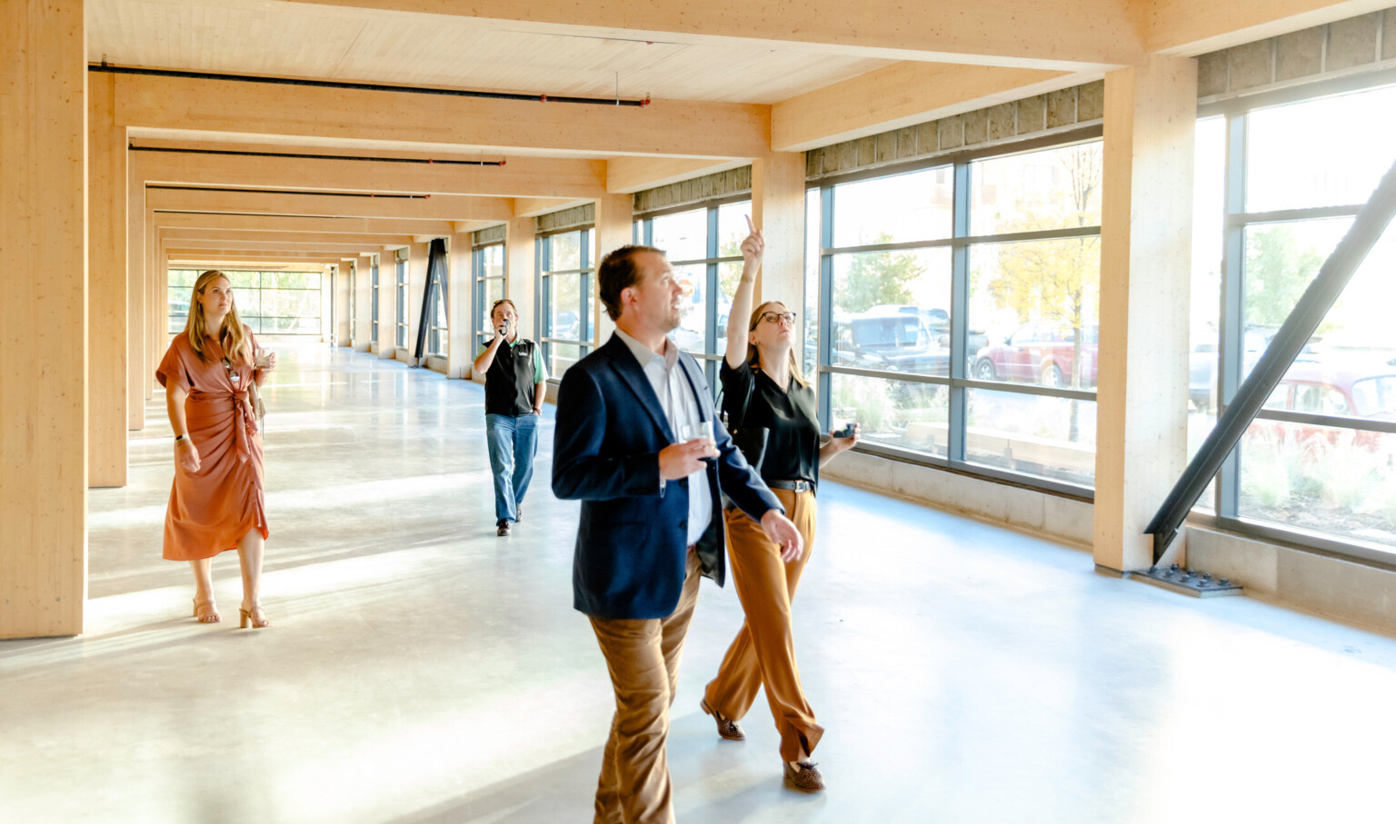 Multiple business people walking through a hallway with windows on the right side