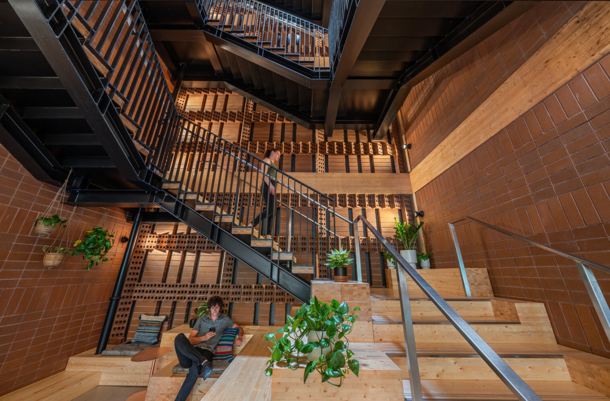 Stairway of a modern mass timber office building; bottom floor community space with benches and greenery
