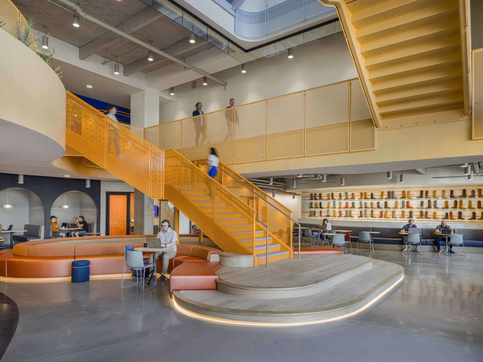 Interior of and office building showing a multilevel common space with orange staircase and a large landing filled with tables and chairs