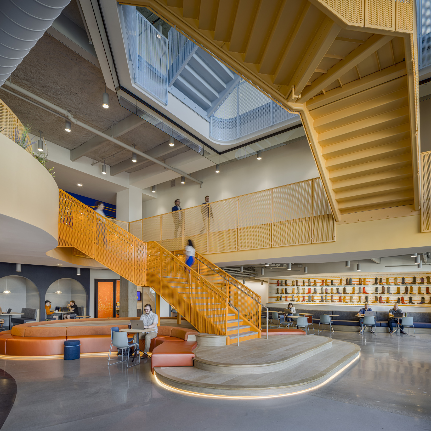 Interior of and office building showing a multilevel common space with orange staircase and a large landing filled with tables and chairs