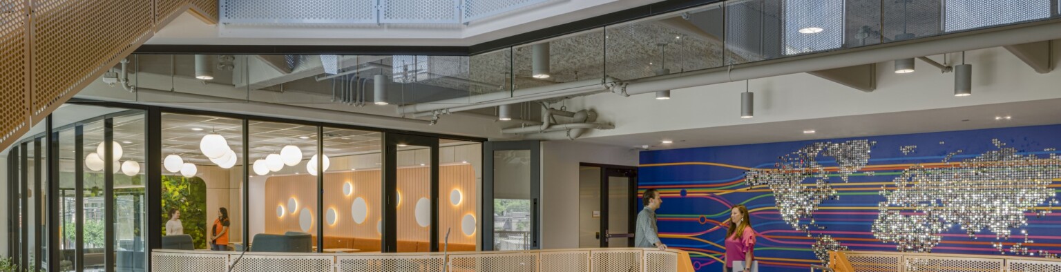 fun and colorful workplace with a central staircase below a skylight; experiential office graphics define the space, a map the world mural in the background