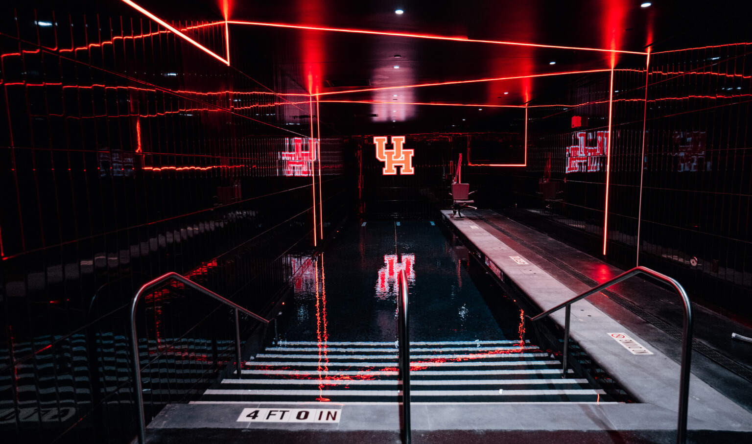 University of Houston football operations center therapeutic recovery pool; very dark room lit by linear led lighting; LED UH at the back wall of the pool room