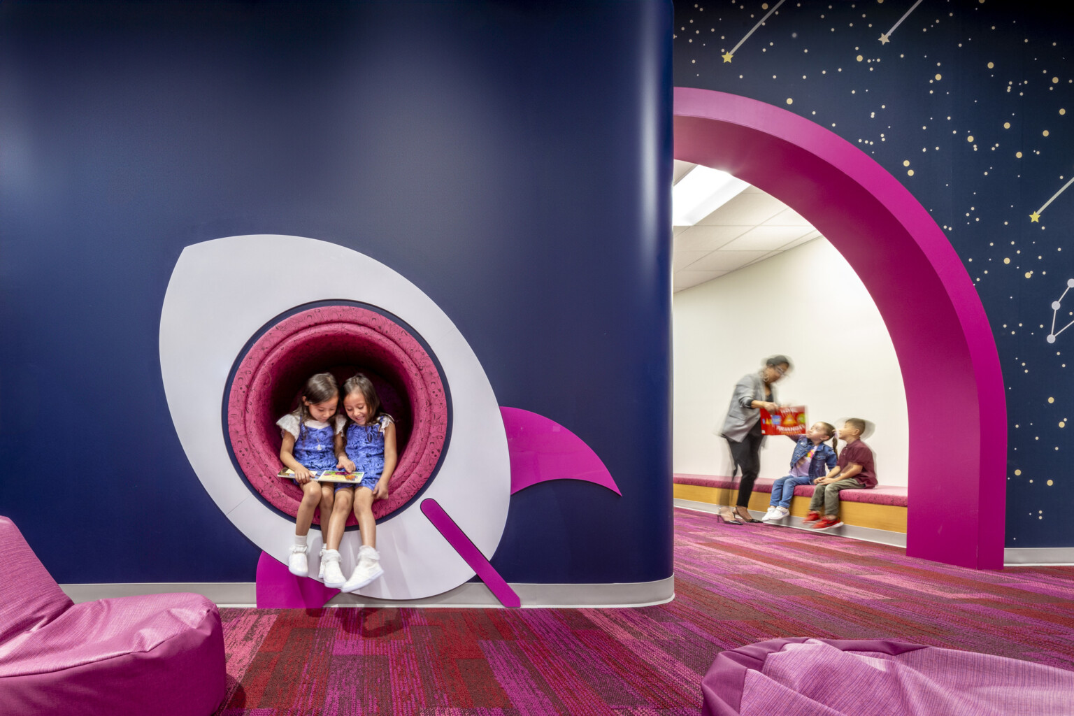 kids reading a book in a cutout window of a space ship mural. Blue walls with pink accents at a early excellence academy. kids reading a book in a cutout window of a space ship mural. Blue walls with pink accents at a early excellence academy.