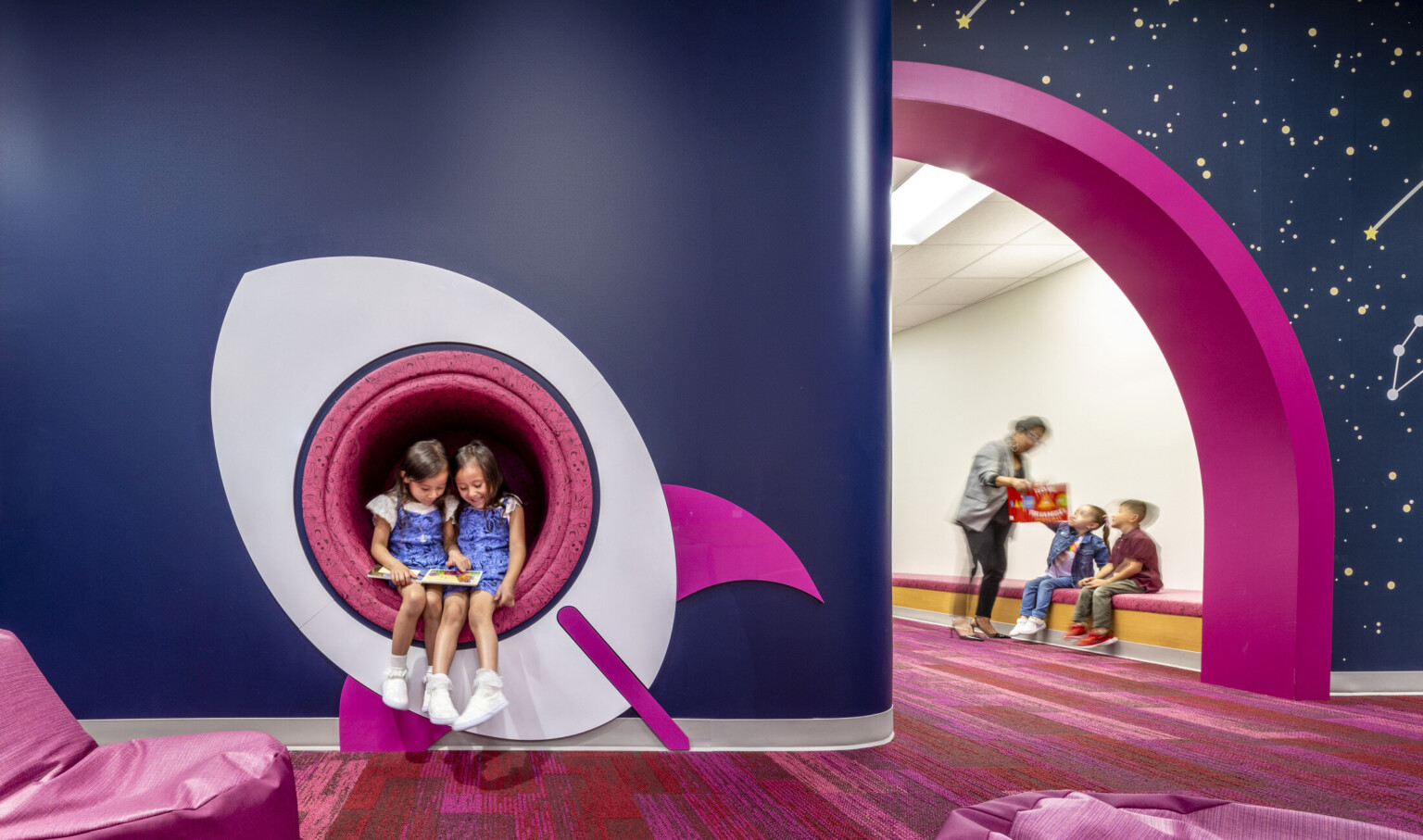 kids reading a book in a cutout window of a space ship mural. Blue walls with pink accents at a early excellence academy. kids reading a book in a cutout window of a space ship mural. Blue walls with pink accents at a early excellence academy.