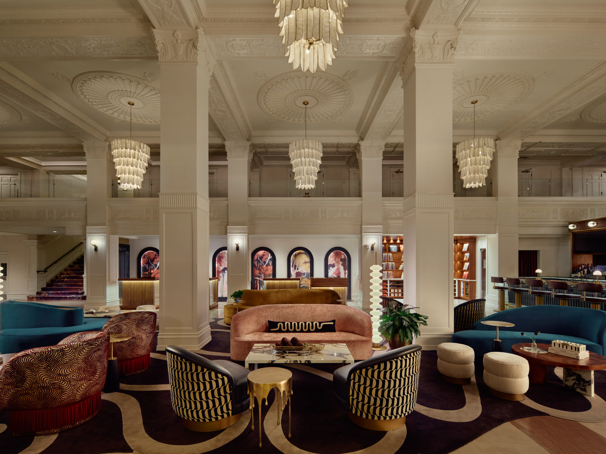 Gunter Hotel lobby lounge with jewel-toned seating, original columns and rosette ceiling, softly glowing chandeliers overhead, check-in desk in the background, and the Keystone Club bar and vinyl library to the right.