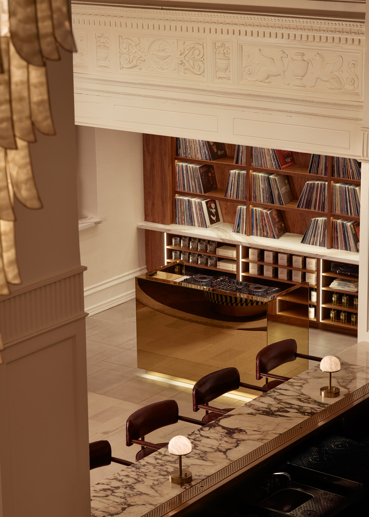 Elevated view of the Gunter Hotel’s gold DJ booth and record library, with a glimpse of the Keystone Club bar and a chandelier above.