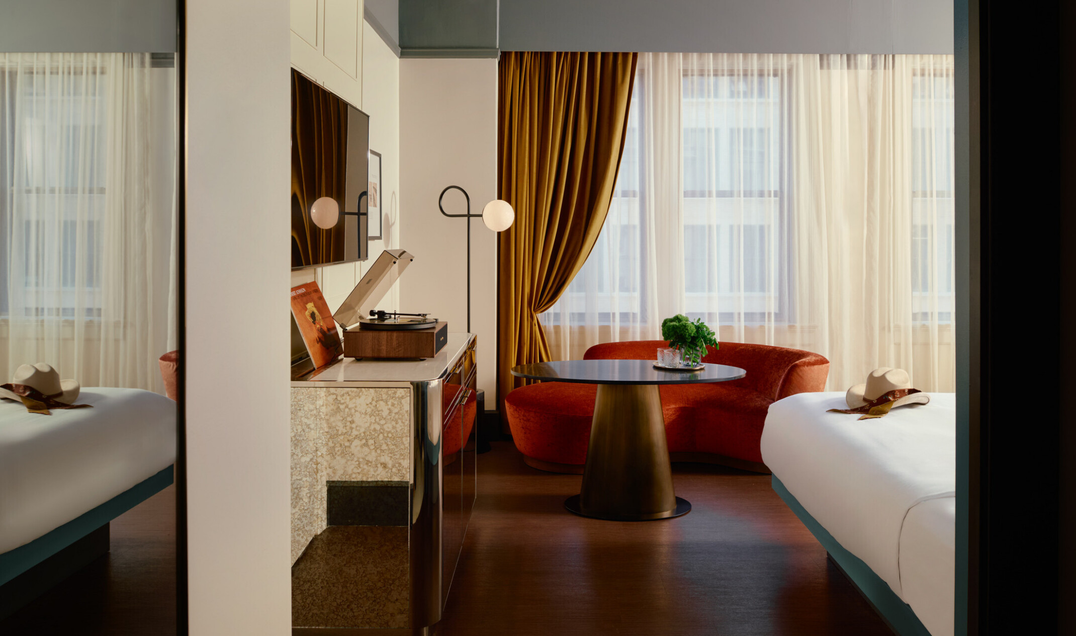 A Gunter Hotel guestroom with a turntable and Robert Johnson’s record on the credenza, a terracotta curved couch and brass table by the window, and the edge of the bed.