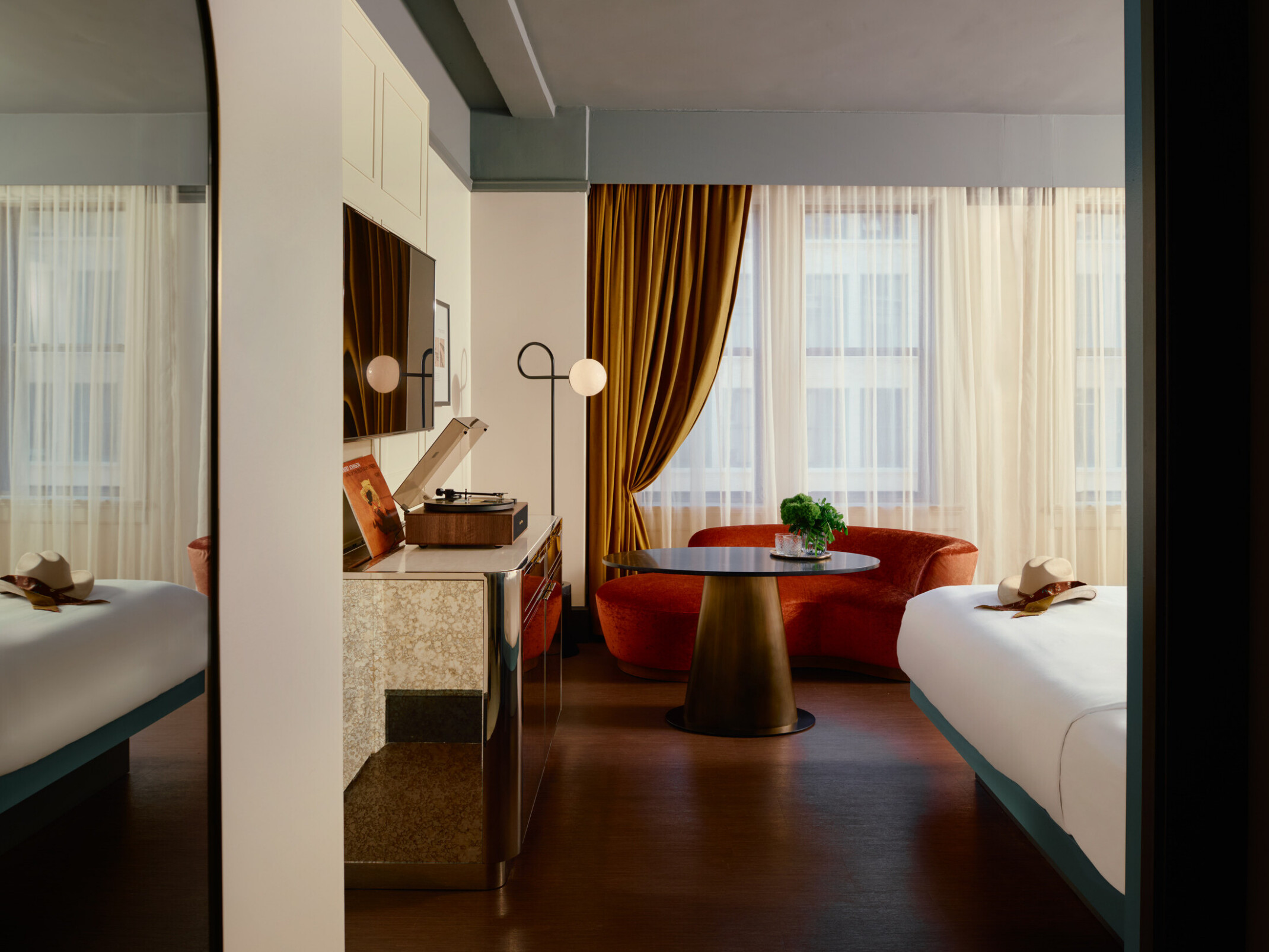 A Gunter Hotel guestroom with a turntable and Robert Johnson’s record on the credenza, a terracotta curved couch and brass table by the window, and the edge of the bed.