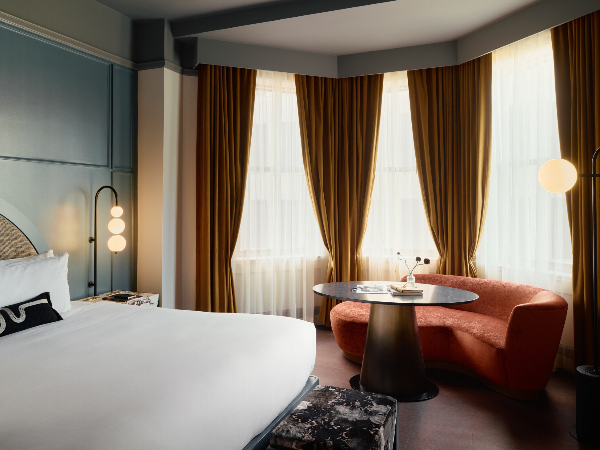 Gunter Hotel guestroom with a half-domed window dressed in floor-to-ceiling curtains and mustard velvet drapes beside a teal headboard wall.