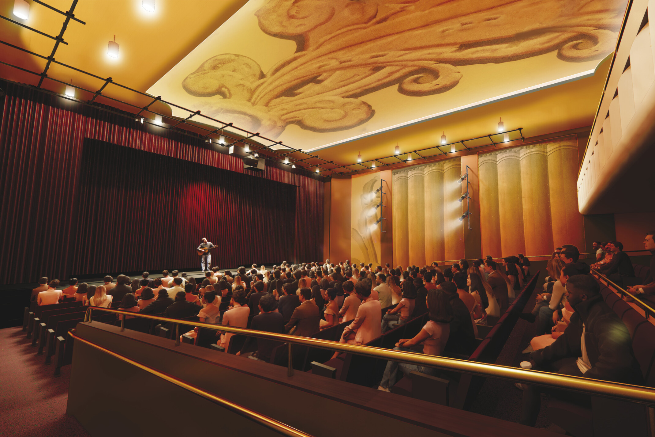 A large auditorium filled with seated audience members facing a stage where a person is speaking or performing. The space features warm amber lighting, tall golden panels along the walls, and a decorative ceiling with an ornate design. Dark red curtains frame the stage, and the overall atmosphere is elegant and formal