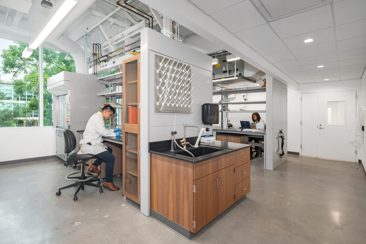 Two scientists in a bright, modern lab—one working at a bench, the other on a laptop; biosciences lab design