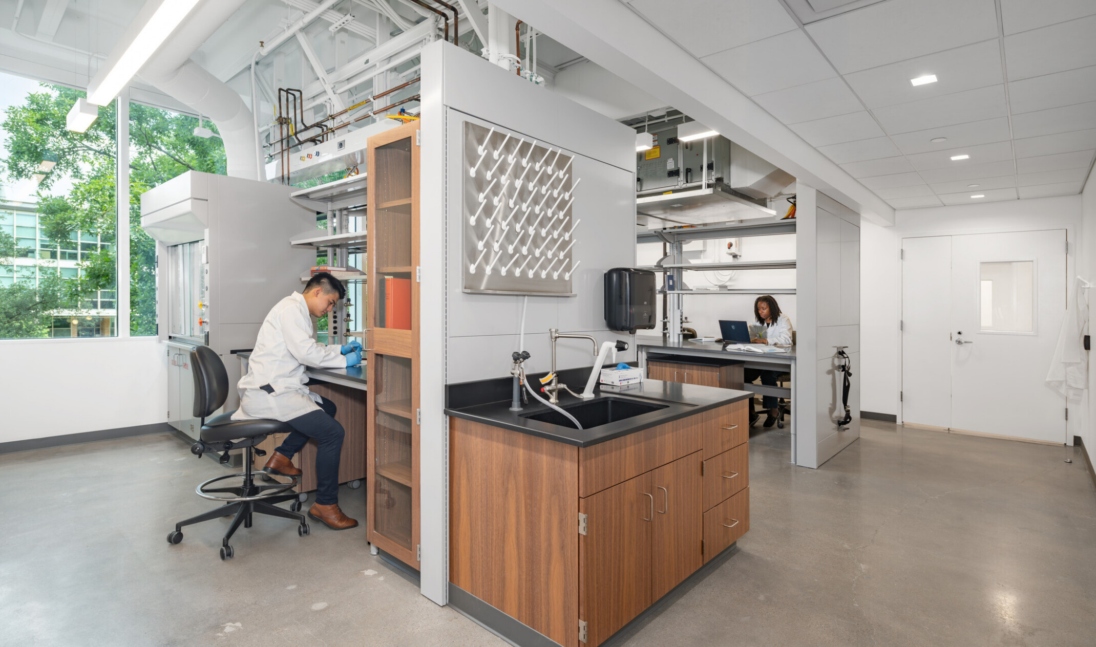 Two scientists in a bright, modern lab—one working at a bench, the other on a laptop; biosciences lab design
