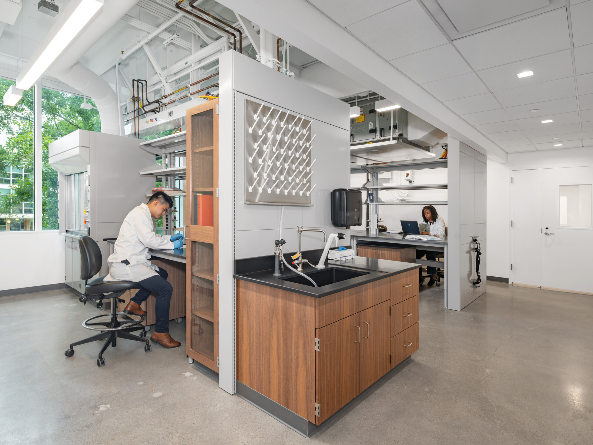 Two scientists in a bright, modern lab—one working at a bench, the other on a laptop; biosciences lab design