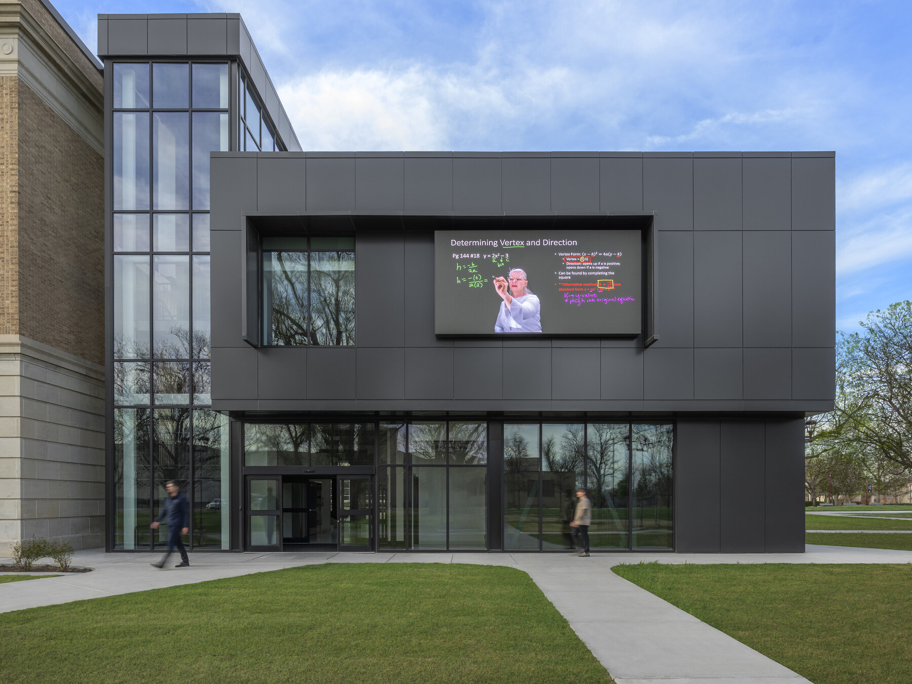 modern building facade with multistory elements; second floor black paneling with building in LED screen